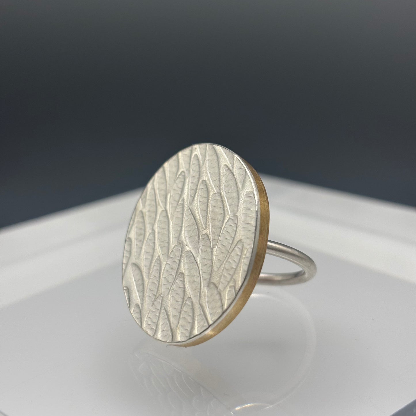 Silver ring with a textured design on a reflective surface