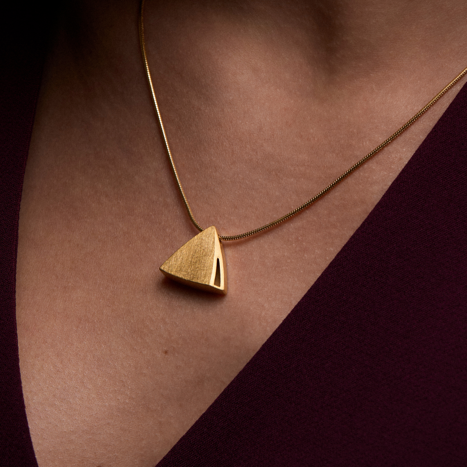 Gold triangle pendant necklace on a person's neck against a dark background