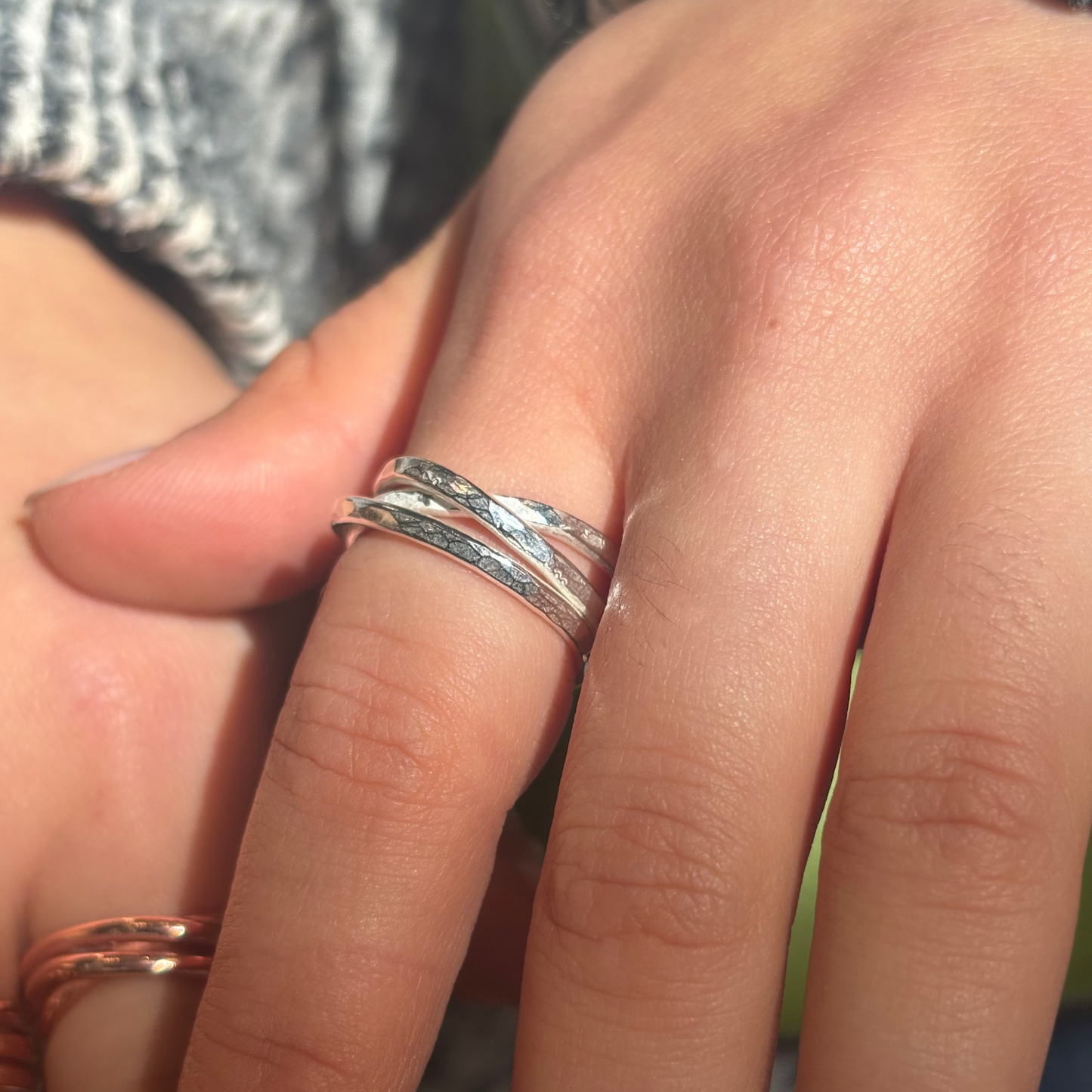 Close-up of a hand wearing two silver rings on a blurred background