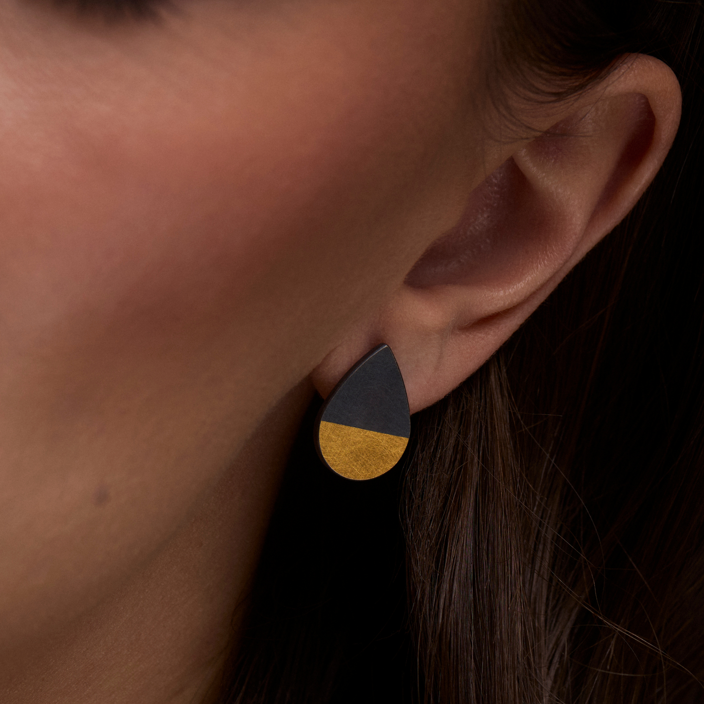 Close-up of an ear wearing a two-tone earring with gold and black colors.